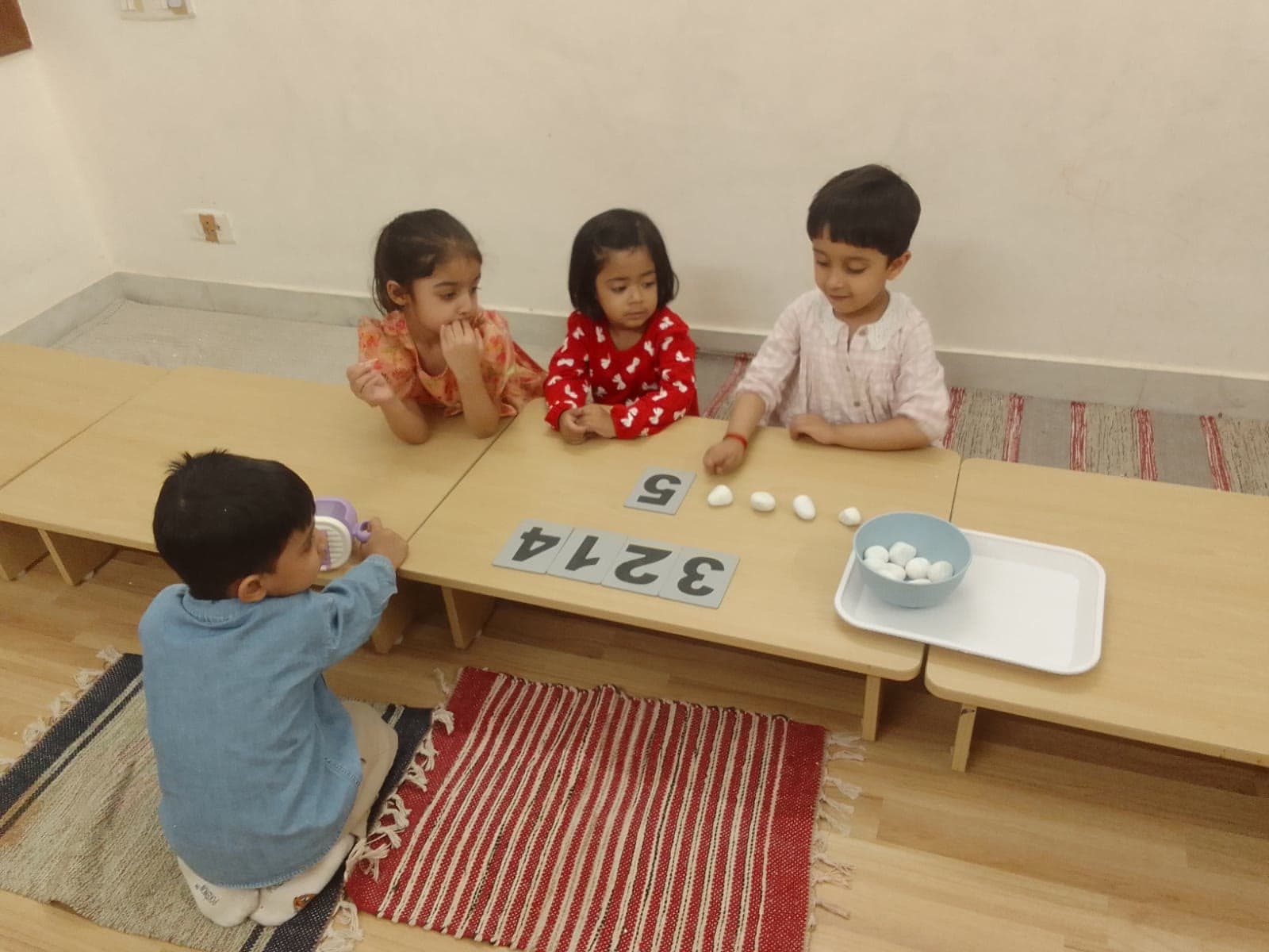 Three children at a low table matching numerals to counted stones on a tray
