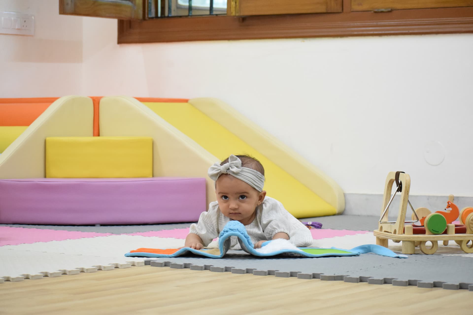 An infant lying on a play mat looking towards the camera, with soft-play shapes behind