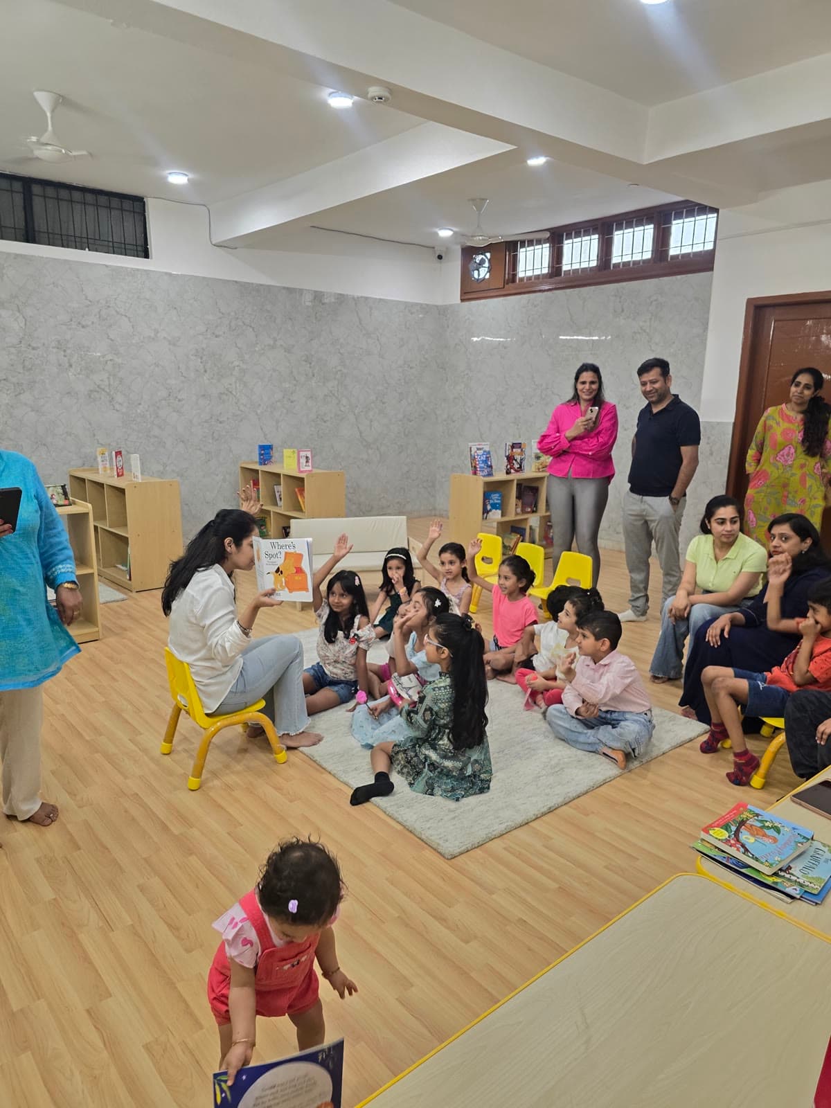 Parents seated along the walls of a classroom watching a child walk across the floor